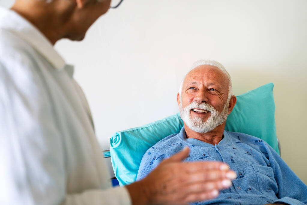 Doctors consulting senior man patient on hospital bed. Talking happy about the diagnose and treatment in modern clinic background. Healthcare and medical insurance concept - Photo, image