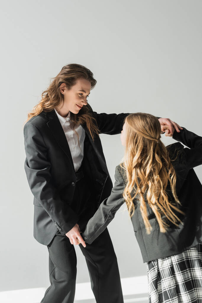 μοντέρνα μητέρα και κόρη, γυναίκα με κοστούμι κρατώντας τα χέρια με μαθήτρια σε σχολική στολή με καρό φούστα, μπλέιζερ, επιχειρηματίας, ετοιμάζεται για το νέο σχολικό έτος, έχοντας τη διασκέδαση  - Φωτογραφία, εικόνα