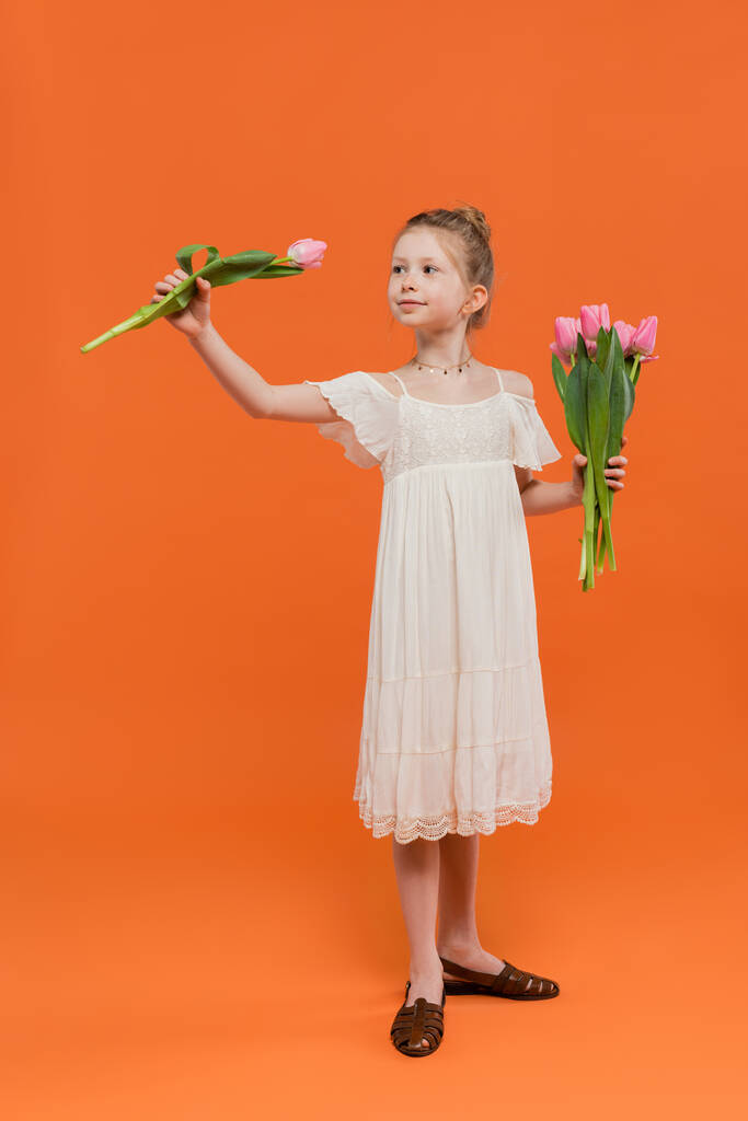 Çiçek buketi, turuncu arka planda pembe laleler tutan beyaz elbiseli küçük kız moda ve tarz konsepti, şık çocuk, canlı renkler, yaz modası, tatlı çocuk  - Fotoğraf, Görsel