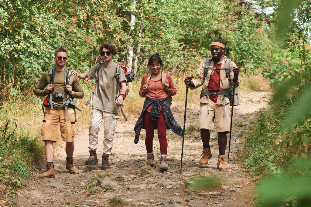 Gruppo di giovani amici multietnici in abiti casual che trasportano zaini mentre camminano insieme nella foresta - Foto, immagini