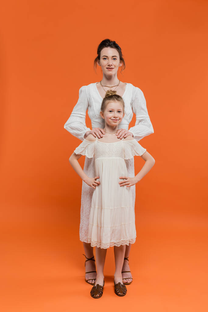 parentalidade moderna, moda de verão, mulher abraçando a filha pré-adolescente e de pé juntos em vestidos de sol brancos no fundo laranja, colagem feminina, família na moda, estilo de verão  - Foto, Imagem