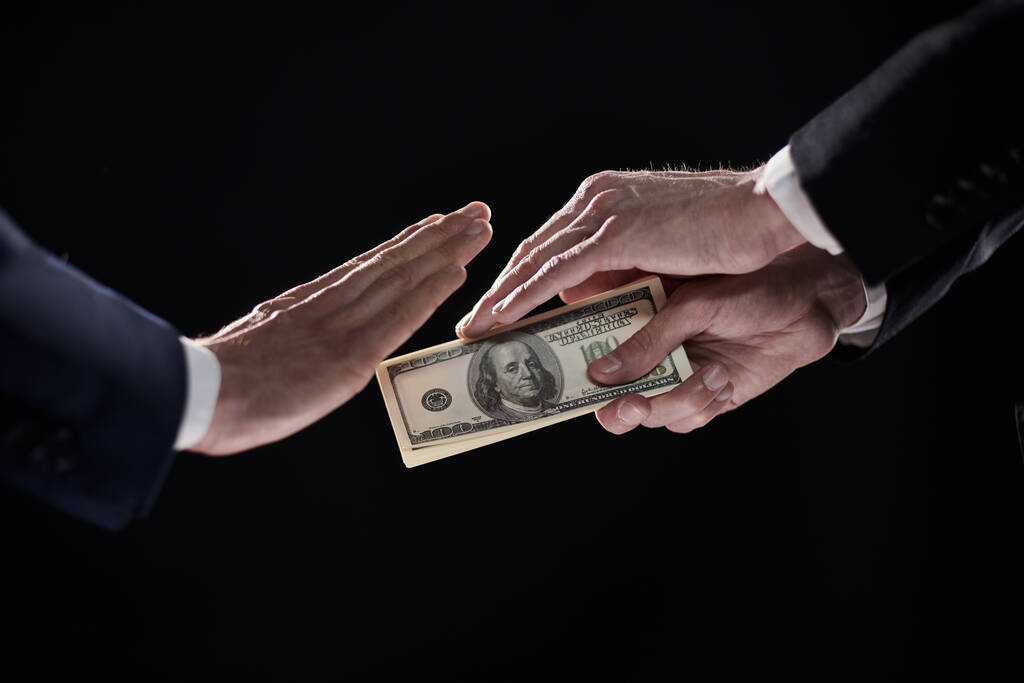 Een mensenhand in een zwart pak houdt een hoop geld uit, wat weigert. Op een zwarte achtergrond - Foto, afbeelding