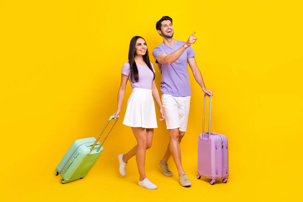 Plná velikost fotografie atraktivní žena muž chůze turisté prst bod kufry nosit trendy fialový vzhled izolované na žlutém pozadí. - Fotografie, Obrázek