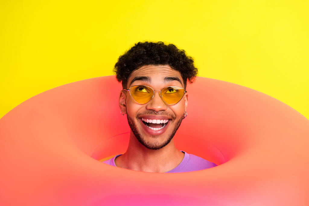 Portrait of funky positive handsome man head through inflatable ring hole look up empty space isolated on yellow color background. - Photo, Image