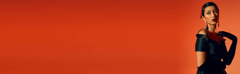Charmante und anmutige asiatische Frau im eleganten Frühlingsoutfit auf rotem Hintergrund, brünettes Haar, fettes Make-up, lange Handschuhe, schwarzes Kleid, trendiges Frühjahrskonzept, Banner - Foto, Bild