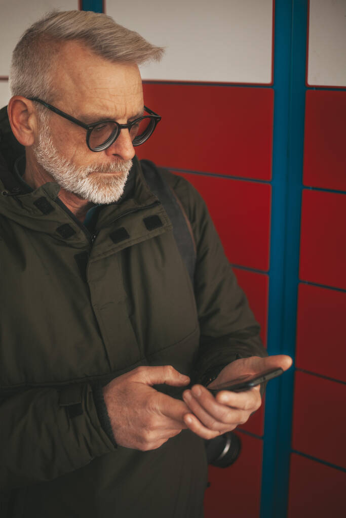 Hombre mayor con teléfono inteligente y aplicación cerca de la máquina de entrega postal. Terminal de autoservicio Express. - Foto, Imagen