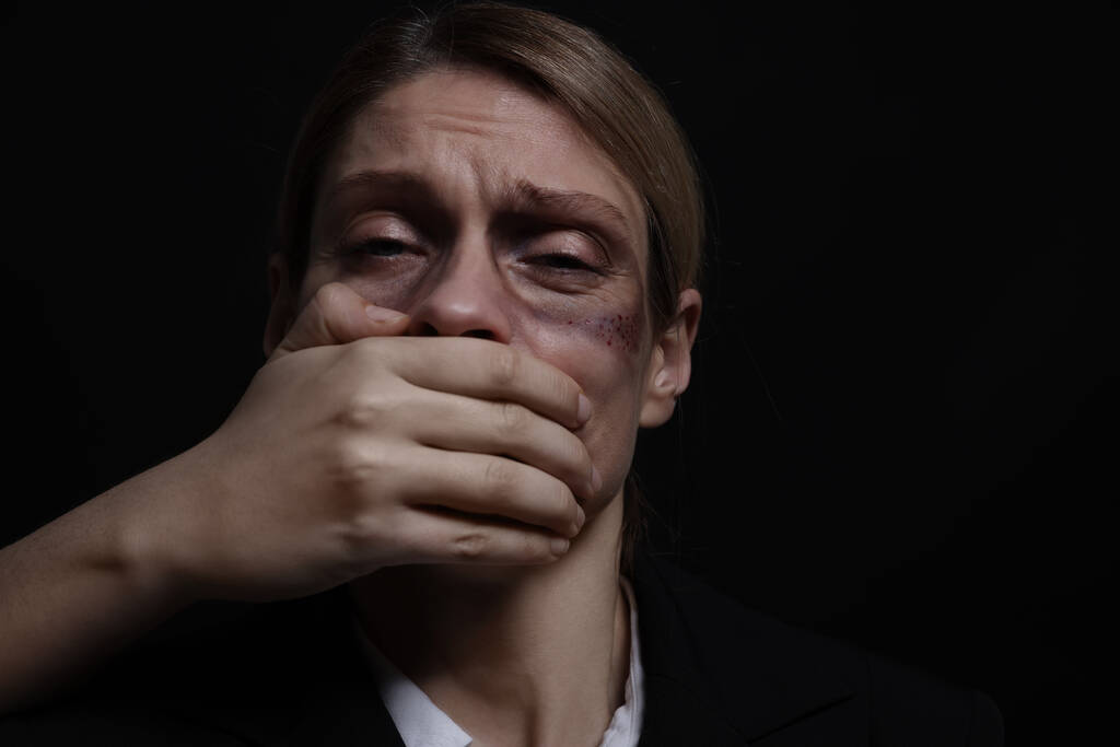 De ontvoerder bedekt de mond van een vrouw die gegijzeld is op een donkere achtergrond. Ruimte voor tekst - Foto, afbeelding