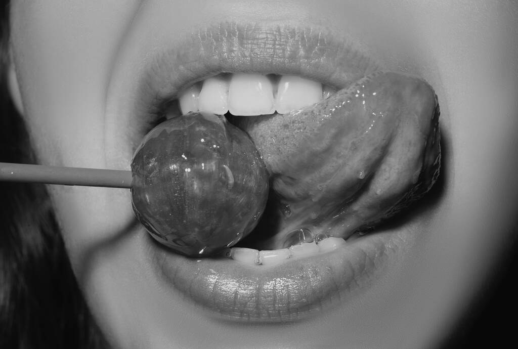 Closeup female lips with pink lipgloss holding in mouth red lollipop candy. Lollipop on a face - Photo, Image