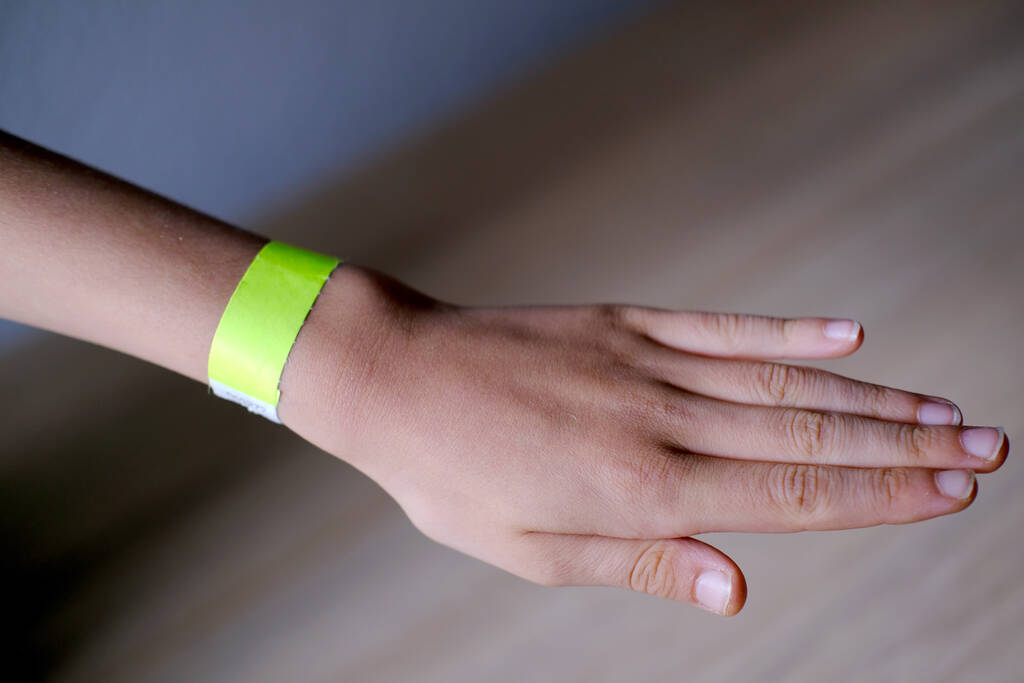 close-up of neon yellow paper bracelet on the male arm of child clinic patient, check tape with entry number on hand of middle-aged european man, event ticket concept - Photo, Image