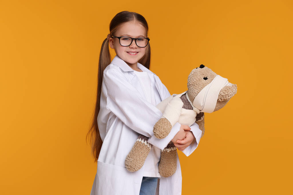 Petite fille en uniforme médical avec ours jouet sur fond jaune - Photo, image