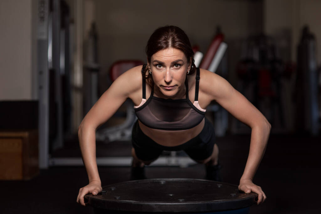 Jeune femme faisant des pompes dans la salle de gym sur un hémisphère d'équilibre. - Photo, image
