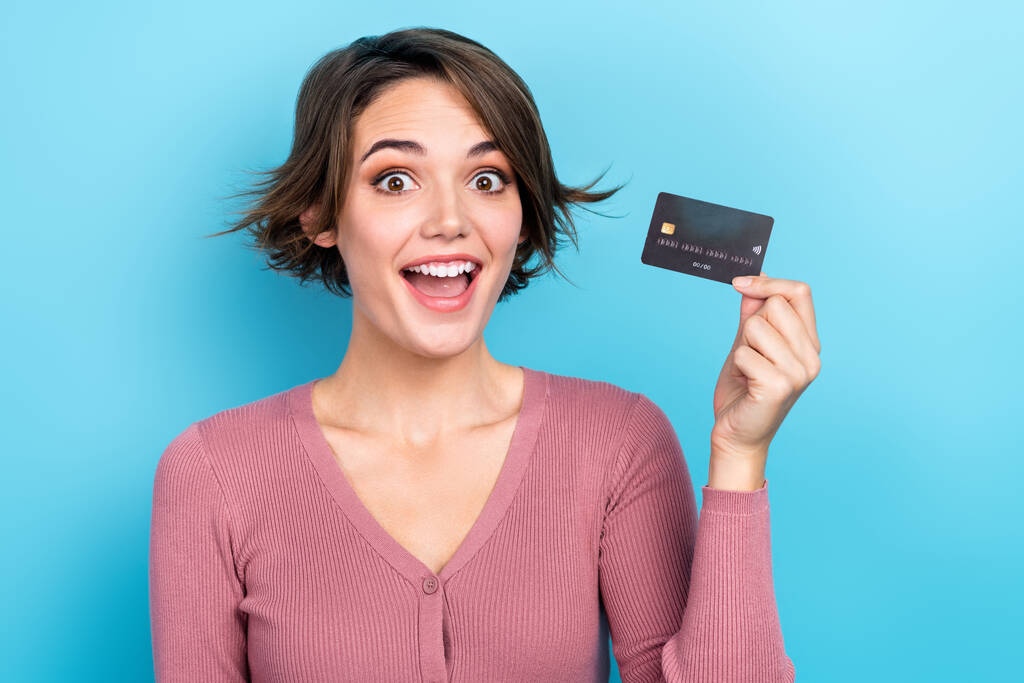 Foto de menina bonita espantada mão segurar cartão de débito de plástico isolado no fundo de cor azul. - Foto, Imagem