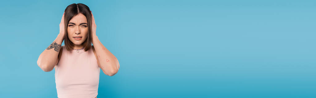 migraine, jeune femme tatouée avec piercing du nez et cheveux courts touchant la tête tout en souffrant de maux de tête sur fond bleu, génération z, fatigue, stress, bannière  - Photo, image
