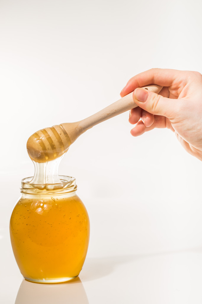 Tarro de miel con rociador de madera aislado sobre fondo blanco
 - Foto, Imagen