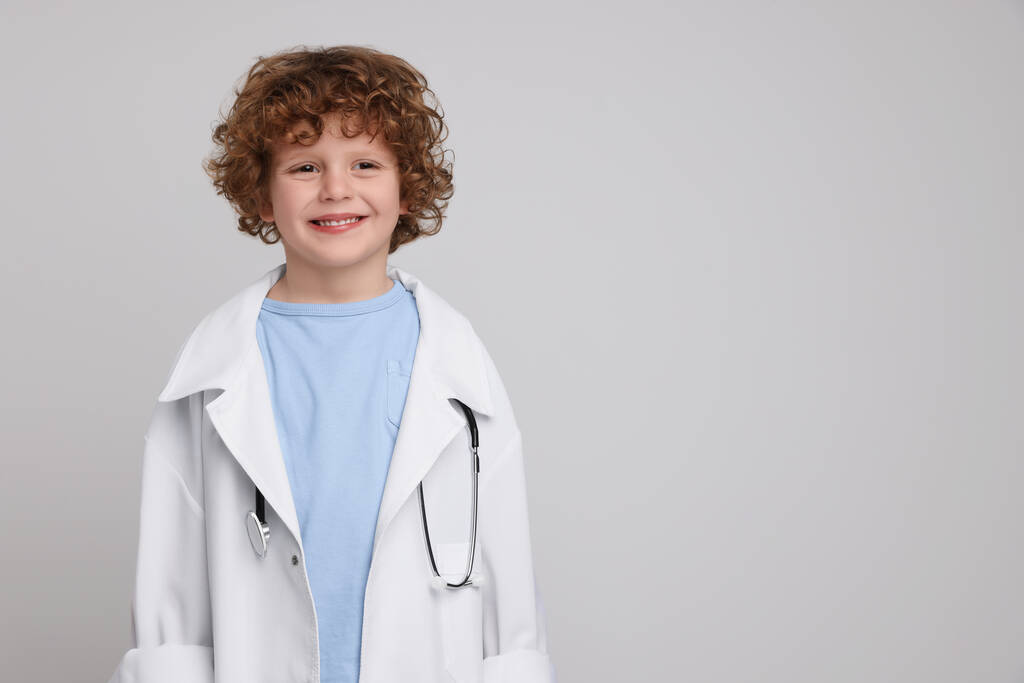 Little boy in medical uniform with stethoscope on light grey background. Space for text - Photo, Image