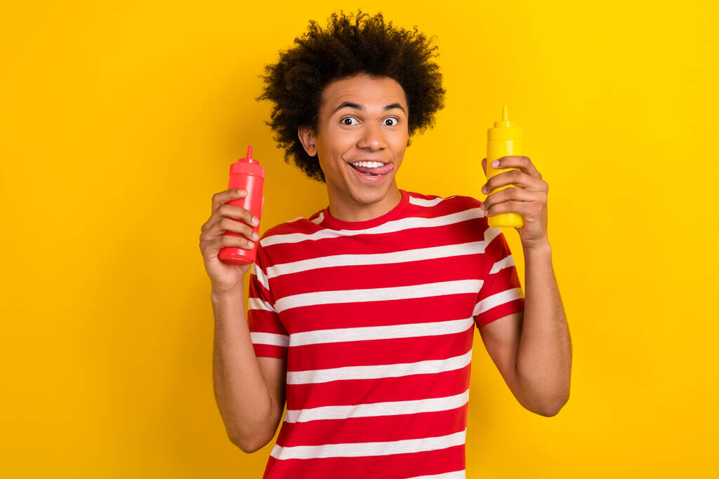 Фото сложного веселого парня в полосатой футболке, выбирающего желтый цвет пищевого соуса. - Фото, изображение