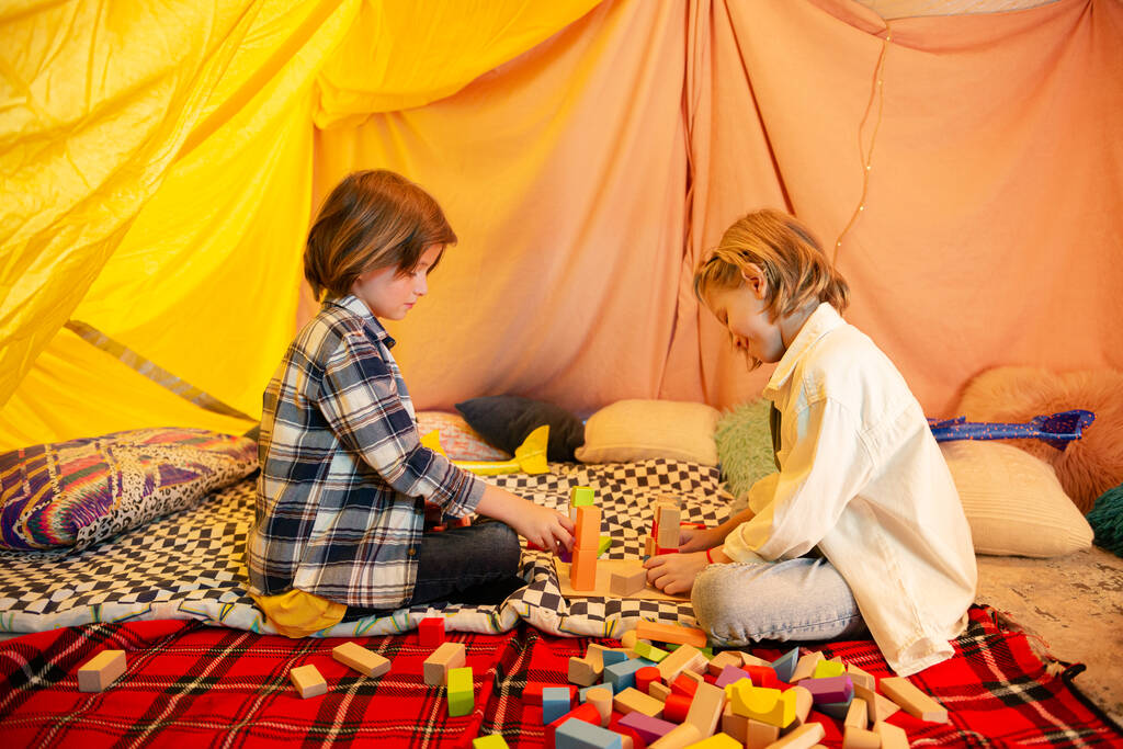 Two young boys are messing around with toy airplanes inside a big blanket tent which has very bright lighting and is decorated in a very modern way to create a comfortable atmosphere. Portrait - Photo, Image