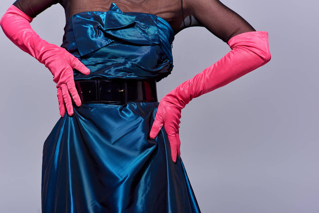 Widok na modną młodą kobietę w sukience koktajlowej i różowych rękawiczkach dotykającą bioder i stojącą odizolowaną na szarej, nowoczesnej generacji koncepcji mody z, detale, pasek, kobiece - Zdjęcie, obraz
