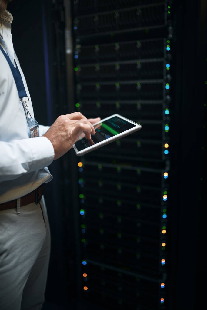 Keeping all data safe and secure. Closeup shot of an unrecognisable man using a digital tablet while working in a server room - Photo, Image