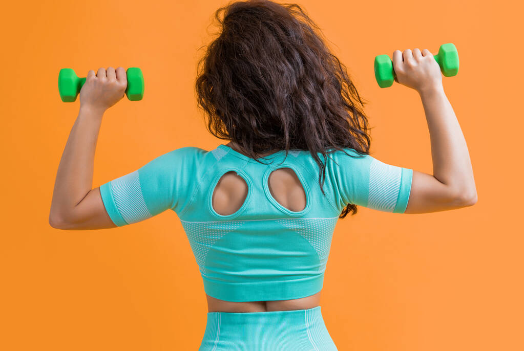 fitness woman do weightlifting exercise with dumbbell, back view. fitness woman do weightlifting exercise isolated on yellow background. fitness and sport. - Photo, Image