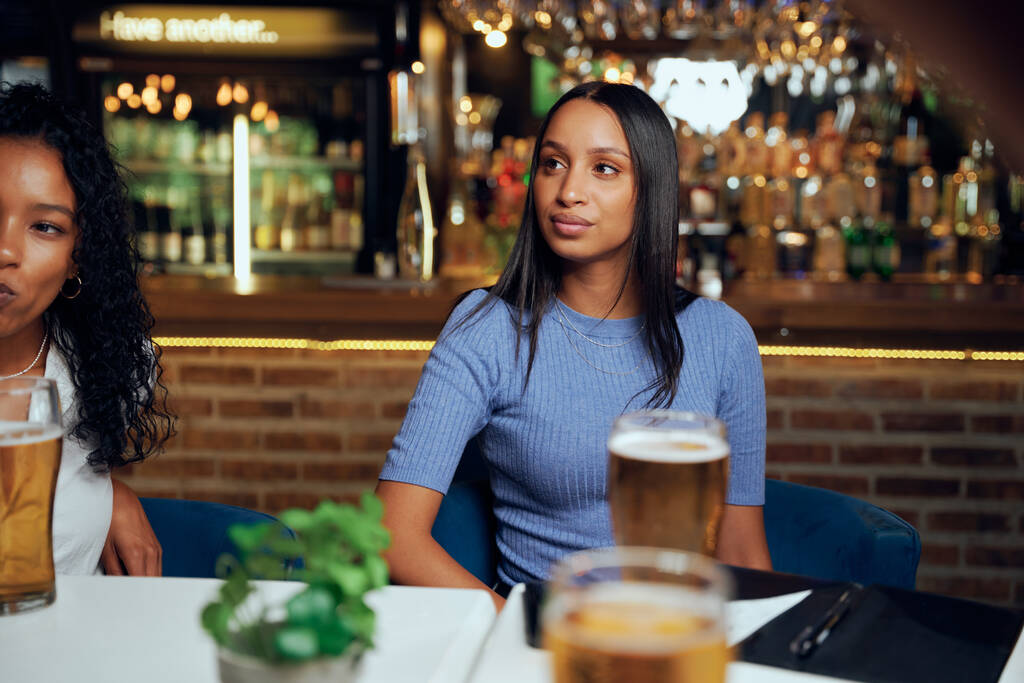 Jeunes femmes portant des vêtements décontractés regardant loin tout en étant assis à table avec des bières et facture au restaurant - Photo, image
