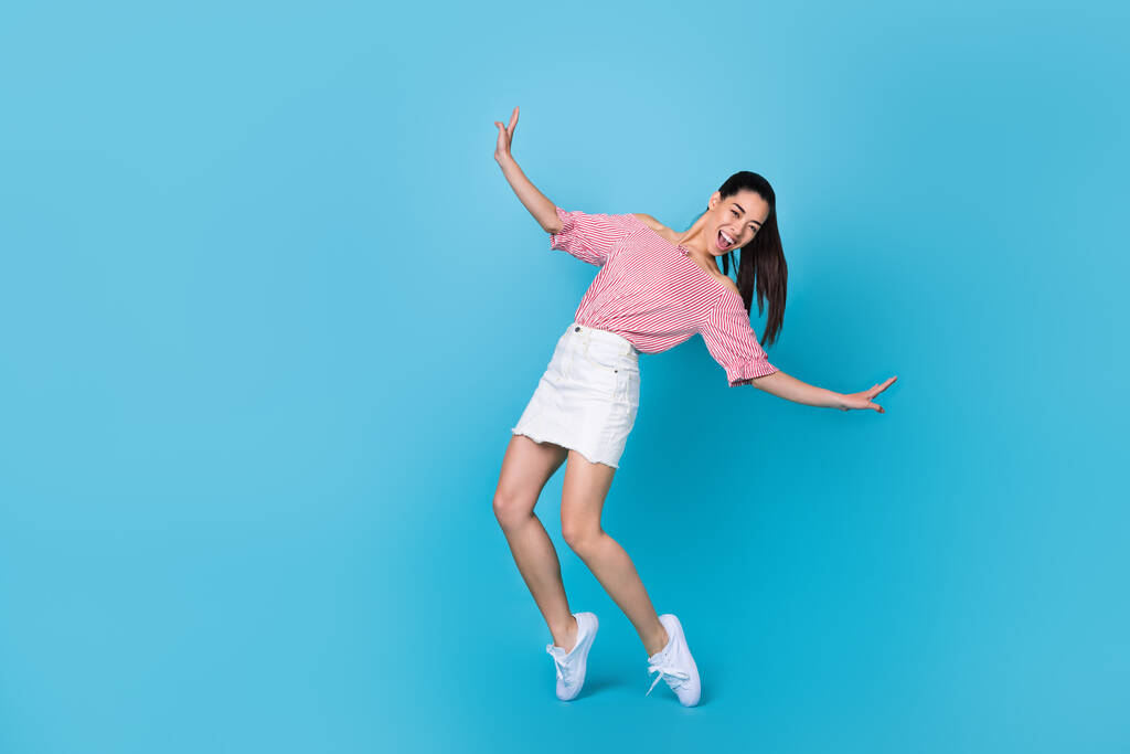 Celotělová fotografie mladé korejské dívky pobyt tipy padající nebezpečí neopatrné slaví pózování nové oblečení izolované na modrém pozadí. - Fotografie, Obrázek