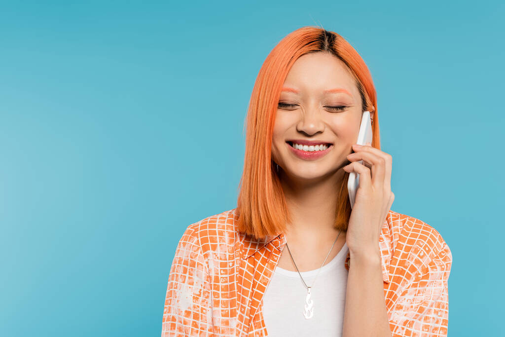 phone call, positivity, joyful and young asian woman with dyed hair and closed eyes talking on smartphone on blue background, mobile phone, youth culture, digital age, generation z - Photo, Image