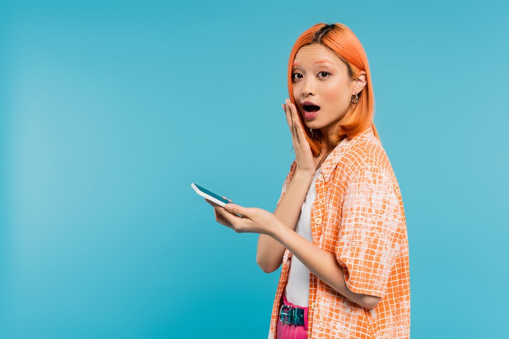 驚くべき顔ソーシャルメディアの影響力青の背景にスマートフォンを使って髪を染めた若いアジアの女性携帯電話若者文化デジタル時代メッセージ世代z - 写真・画像