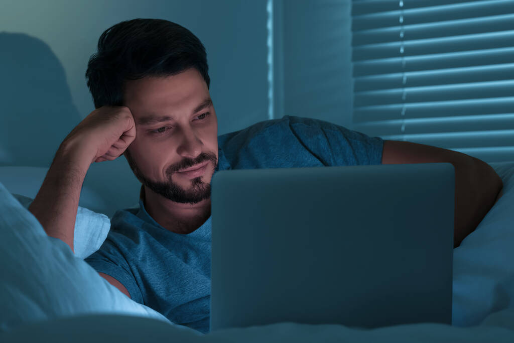 Mies käyttää läppäriä sängyssä öisin. Internet-riippuvuus - Valokuva, kuva