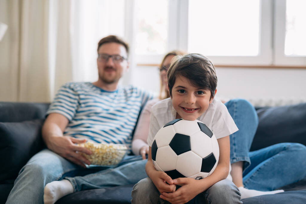 Szczęśliwy chłopiec jest podekscytowany, aby obejrzeć mecz piłki nożnej z rodzicami. - Zdjęcie, obraz