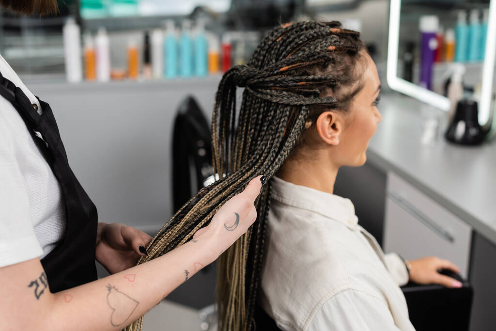 професіонал з волосся, татуйований працівник краси тримає коси жіночого клієнта в салоні, індустрії краси, роботі в салоні, клієнт в салоні, перукарні, послуги салону, волосся роблять
  - Фото, зображення