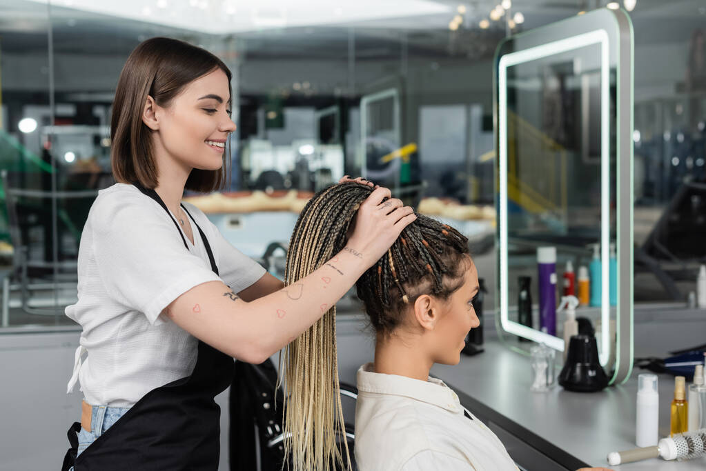 hair make over, cheerful hair stylist lifting hair of female client with braids, salon customer, beauty profession, client satisfaction, hair fashion, hairdo, tattooed, beauty profession  - Photo, Image