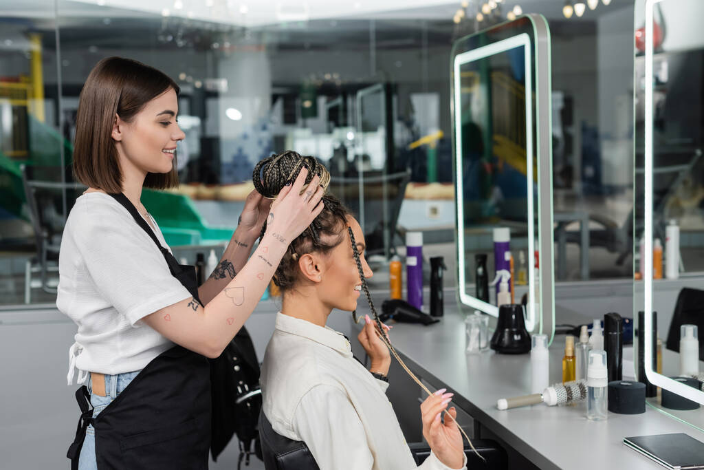 przerobić włosy, szczęśliwy fryzjer robi włosy klientki z warkoczami, wesołe kobiety, zadowolenie klienta, klient w salonie, usługi kosmetyczne, doświadczenie salon, kobiece, tatuaż  - Zdjęcie, obraz