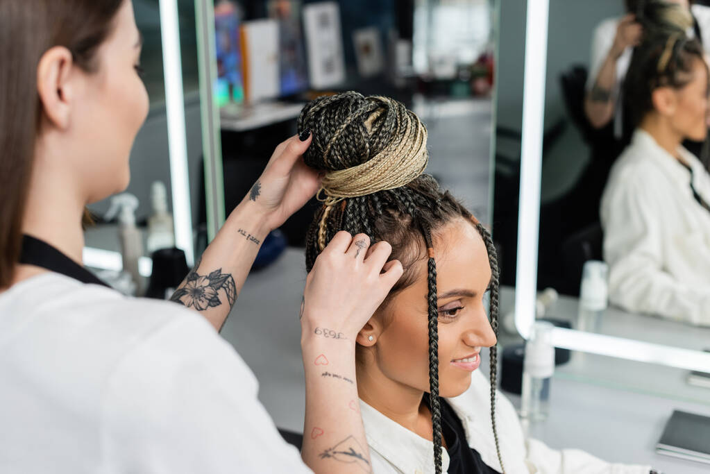 salon experience, tattooed hairdresser doing hair bun to female client with braids, cheerful women, client satisfaction, customer in salon, beauty service, feminine, hair make over, blurred  - Photo, Image