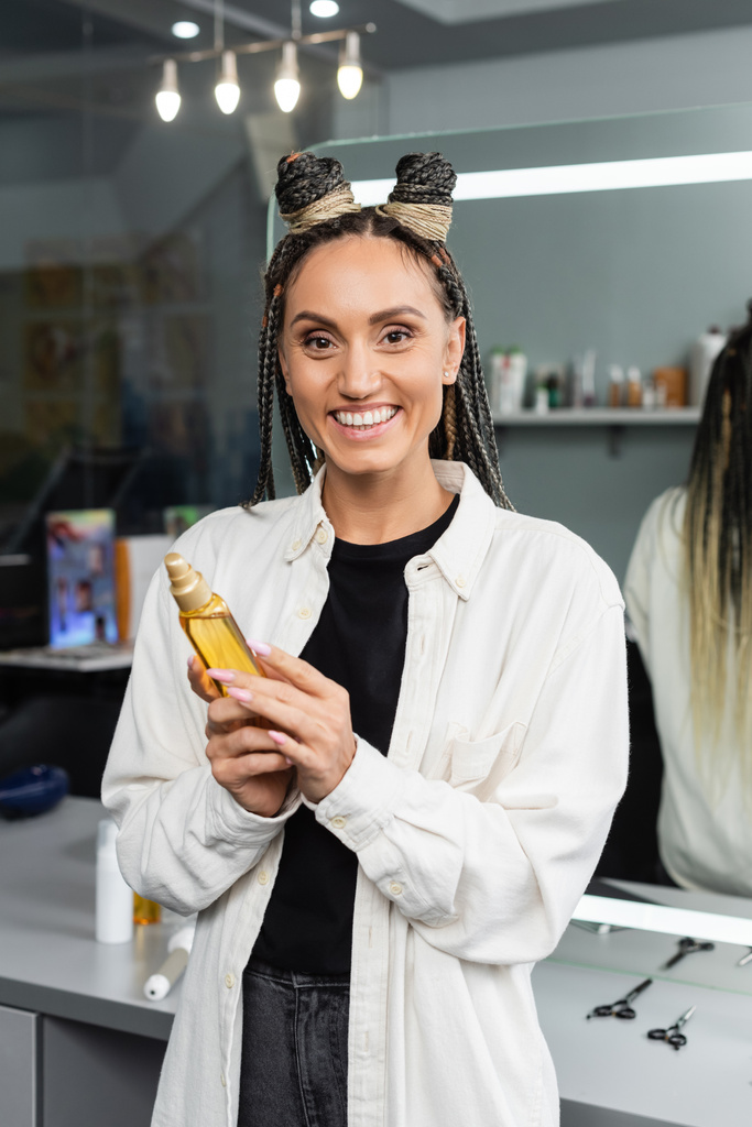 happy woman in beauty salon, joyful client with braids looking at camera, customer satisfaction, hairstyle, female client with braids, holding hair oil, hair buns, braided hair, portrait  - Photo, Image
