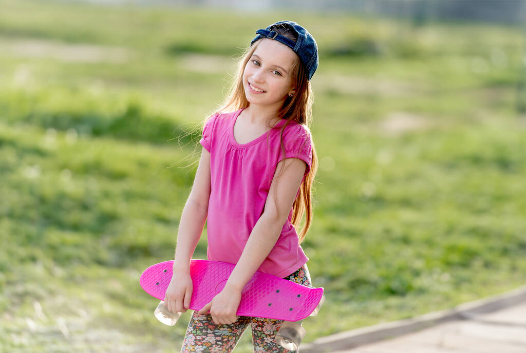 Atrakcyjne dziewczyny nastoletnie z czapką na przytrzymanie jej jasny różowy deska na łyżwach, uśmiechając się - Zdjęcie, obraz
