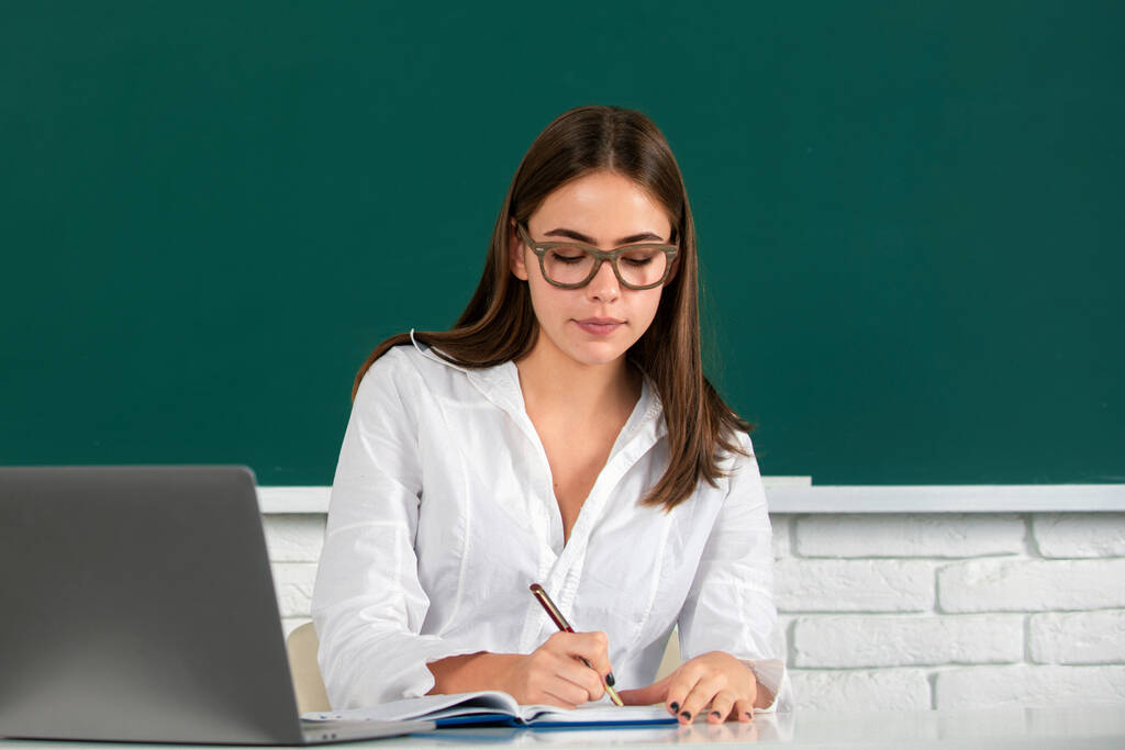 Портрет красивой молодой женщины-студентки с ноутбуком в классе университета. Студентка-красавица. Студентка колледжа на доске. Симпатичная студентка за столом. День студента - Фото, изображение