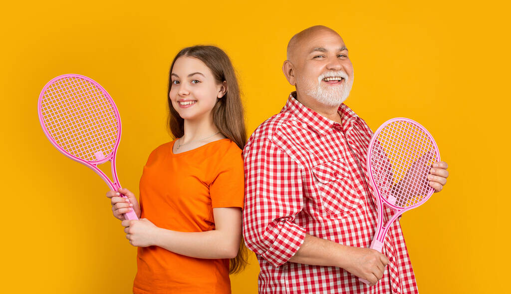 gelukkig tiener kind met grootvader met badminton racket op gele achtergrond. - Foto, afbeelding