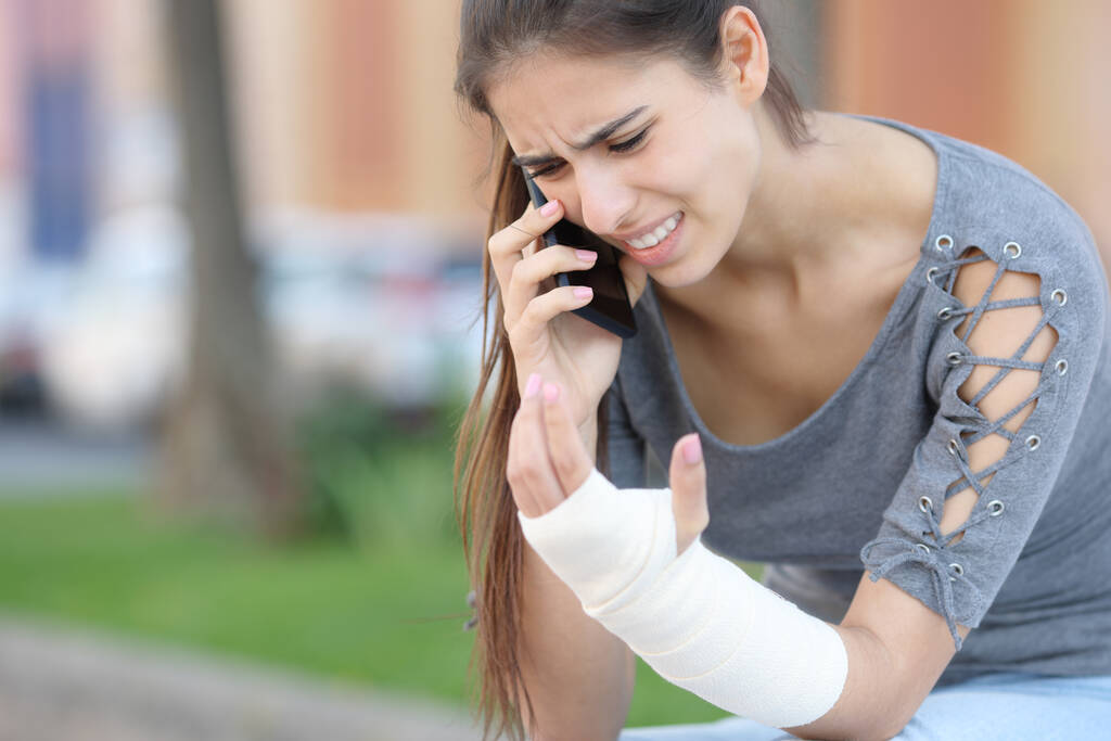 Женщина-выздоравливающая с перевязанной рукой звонит доктору по телефону, сидя на улице - Фото, изображение