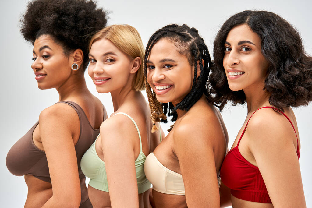Porträt fröhlicher und multiethnischer Frauen in bunten BHs, die in die Kamera schauen, während sie isoliert auf grauen, unterschiedlichen Körpertypen und Selbstakzeptanzkonzepten posieren, multikulturelle Modelle - Foto, Bild