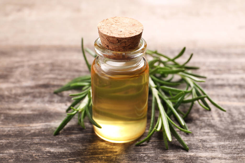 Bottle of essential oil and fresh rosemary on wooden table, closeup - Photo, Image