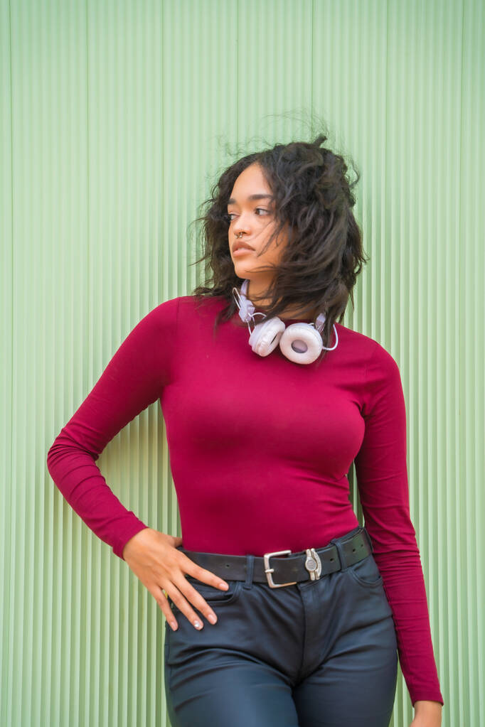 Retrato de mujer latina con auriculares, concepto de tecnología en un fondo verde, estudiante en el campus - Foto, imagen