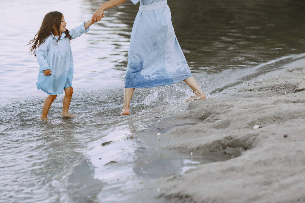 Мама и дочь в одинаковых платьях. Семья играет на берегу реки. - Фото, изображение