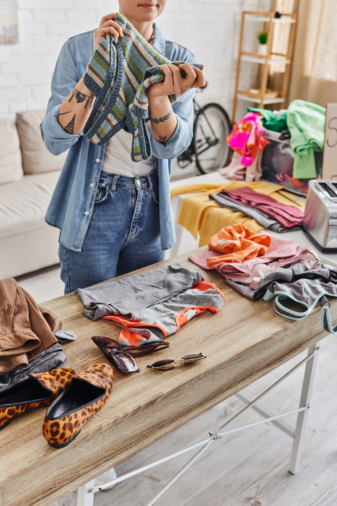 eco-friendly swaps, partial view of tattooed woman with knitted tank top near animal print shoes, sunglasses and casual clothes on table at home, sustainable living and mindful consumerism concept - Photo, Image