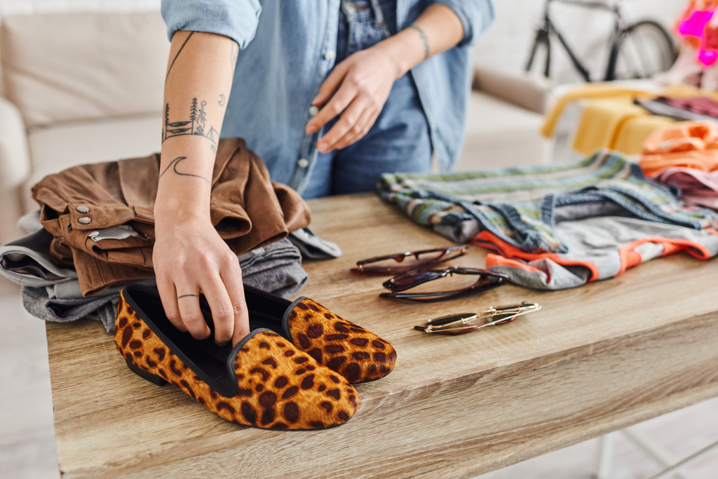 ostříhaný pohled tetované ženy, která klade zvířecí tiskovou obuv na stůl s použitými předměty a slunečními brýlemi, etickou spotřebou, výměnou, udržitelným životem a pozorným konzumním konceptem - Fotografie, Obrázek