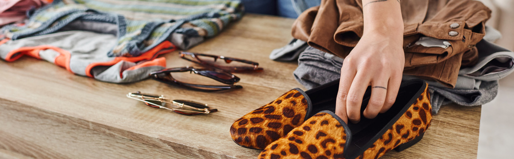 partial view of woman placing fashionable animal print shoes near sunglasses and pre-loved clothes on table at home, eco-friendly swaps, sustainable living and mindful consumerism concept, banner - Photo, Image