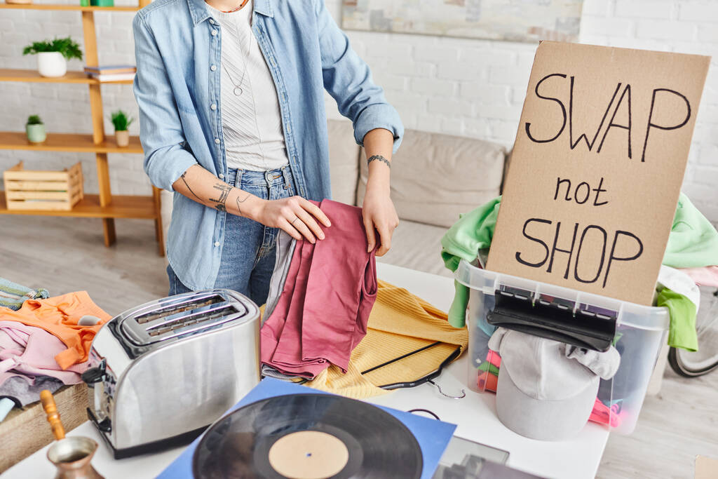 cropped view of tattooed woman with pants near vinyl disc, electric toaster, wardrobe items, plastic box and swap not shop card, exchange market, sustainable living and circular economy concept - Photo, Image