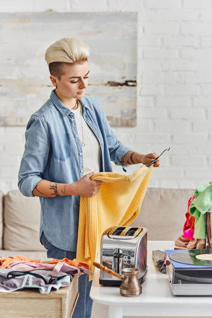 биржевой рынок, татуированная женщина с модной прической с желтым джемпером рядом со столом с электрическим тостером, виниловым проигрывателем и одеждой, устойчивой жизнью и внимательной концепцией потребительства - Фото, изображение