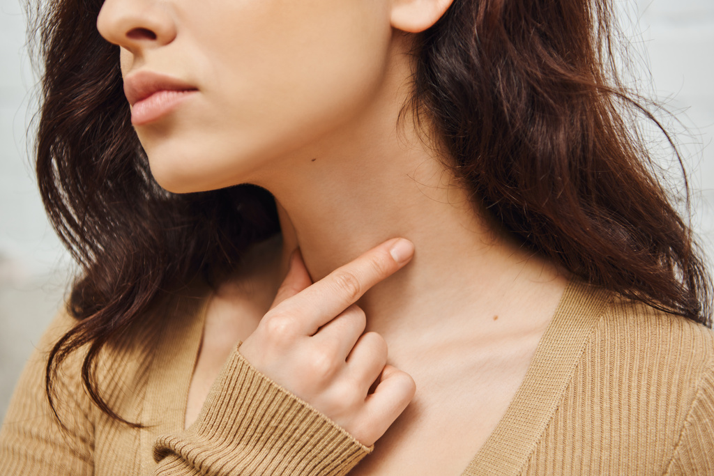 Cropped view of young brunette woman doing self-massage of thyroid gland on neck and lymphatic circulation at home, self-care ritual and holistic wellness practices concept, tension relief - Photo, image