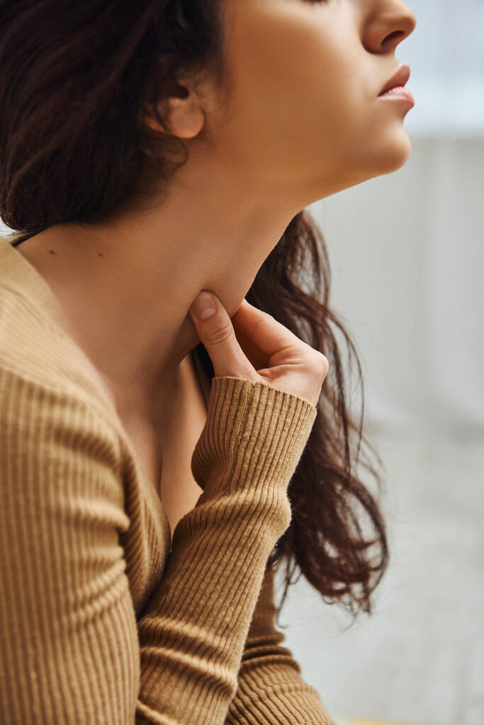 Ausgeschnittene Ansicht einer brünetten jungen Frau im braunen Pullover, die Tyrode bei der Selbstmassage zu Hause am Hals massiert, Selbsthilferitual und ganzheitliches Heilkonzept, ausgleichende Energie - Foto, Bild